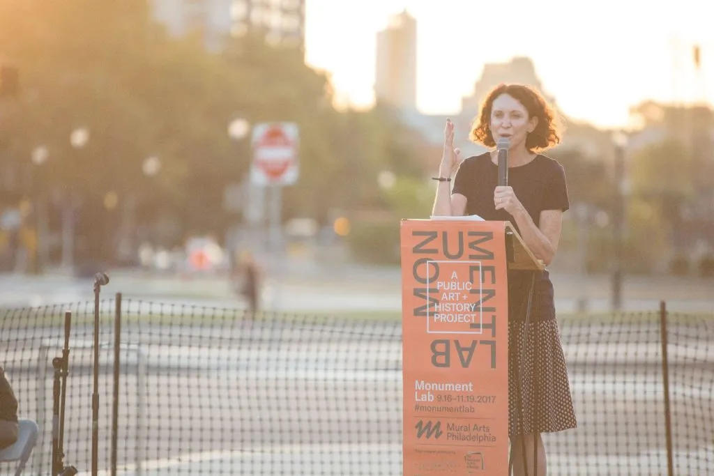 Woman speaking into a microphone at a branded podium with the city in background