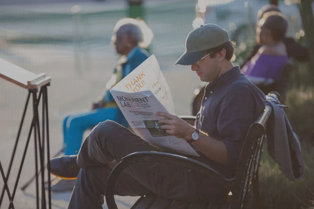 Man reading exhibition newspaper on city bench