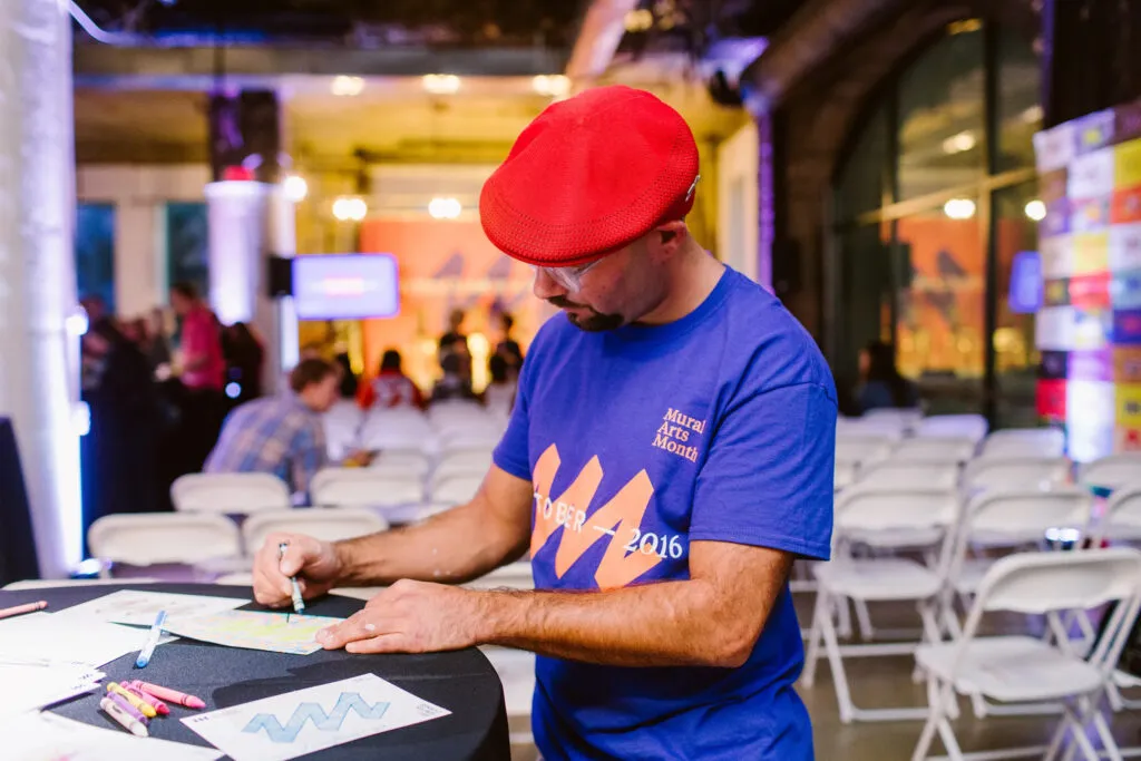 Man wearing Mural Arts Philadelphia blue t-shirt and red hat