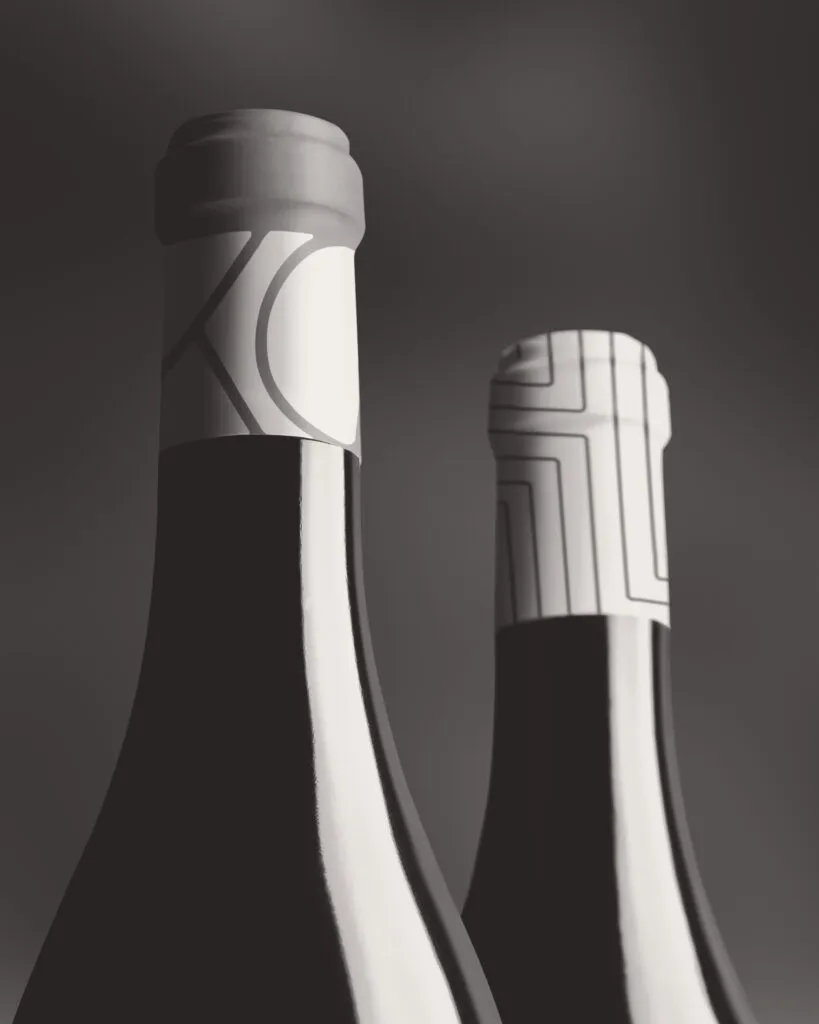 dramatic black and white photo of two wine bottles with branded capsules