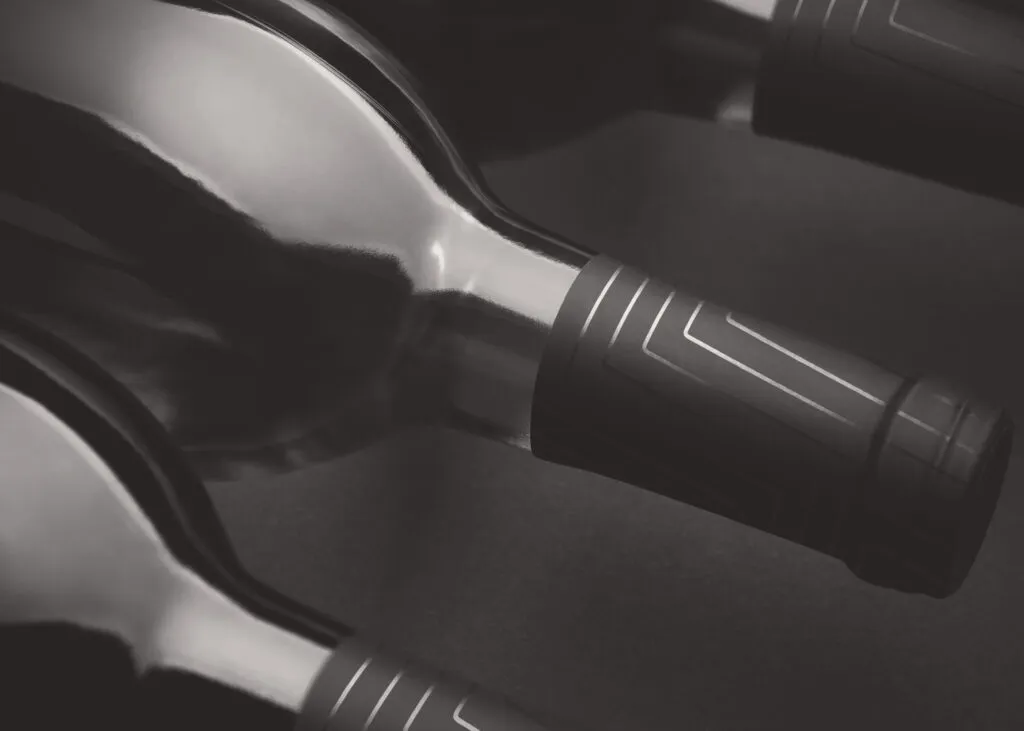 dramatic black and white photo of three wine bottles on their side with branded capsules