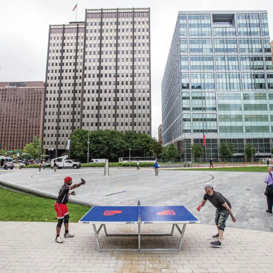 two people in city park playing ping pong on table with printed park logos