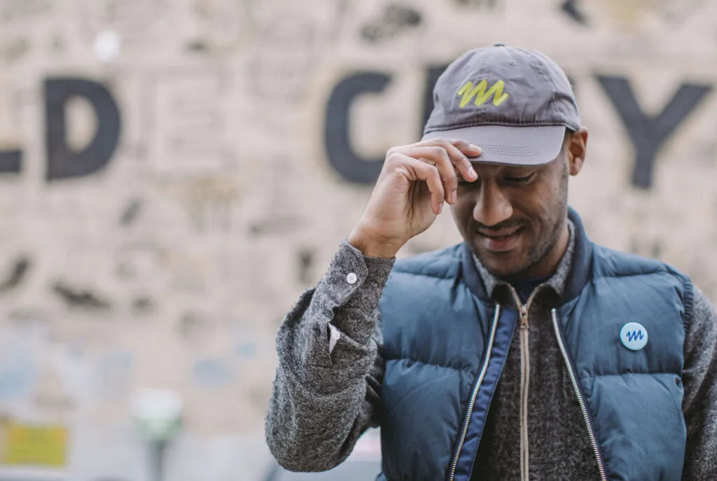 African American man wearing a hat and pin featuring the Mural Arts Philadelphia logo by J2