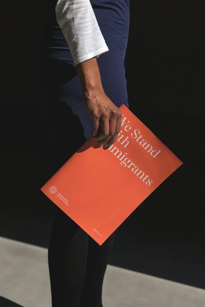 woman holding a bold orange marketing brochure with big serif headline and small logo