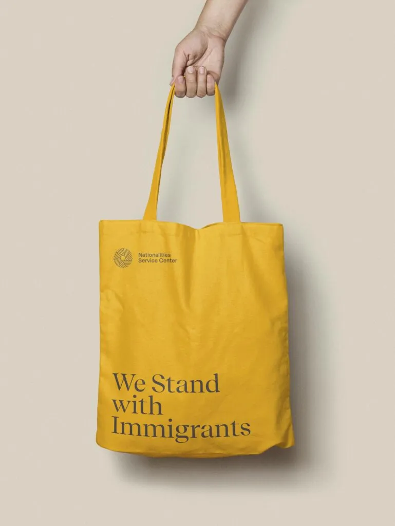 hand holding a yellow tote bag with bold serif tagline and small logo