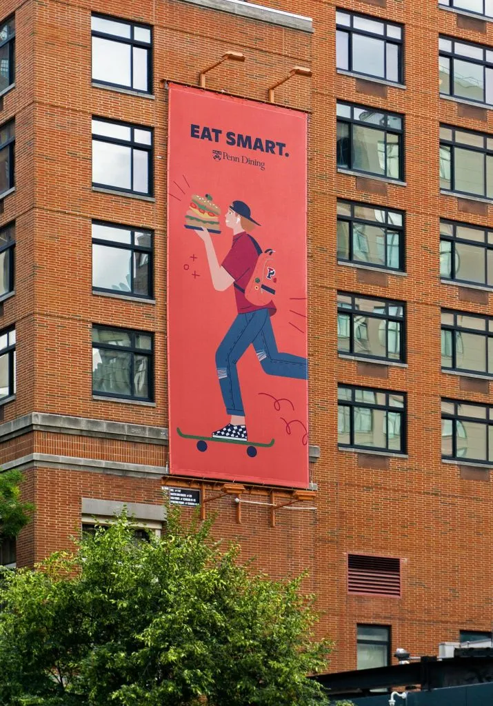 Large outdoor advertisement for college dining program with quirky illustration of student on skateboard eating a huge sandwich