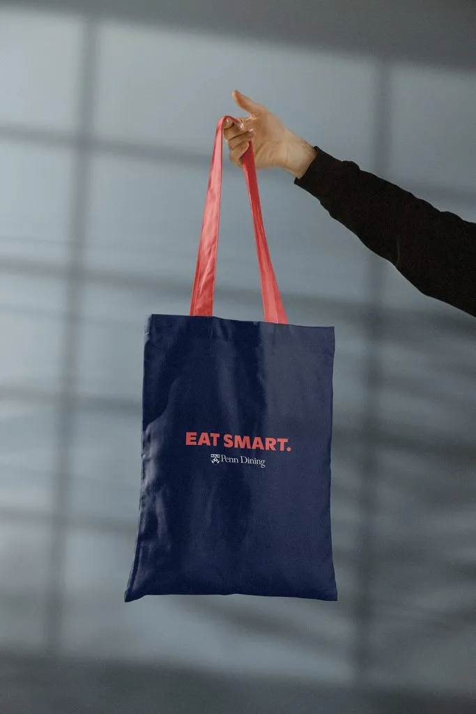 student holding blue tote bag from university dining program with large tagline