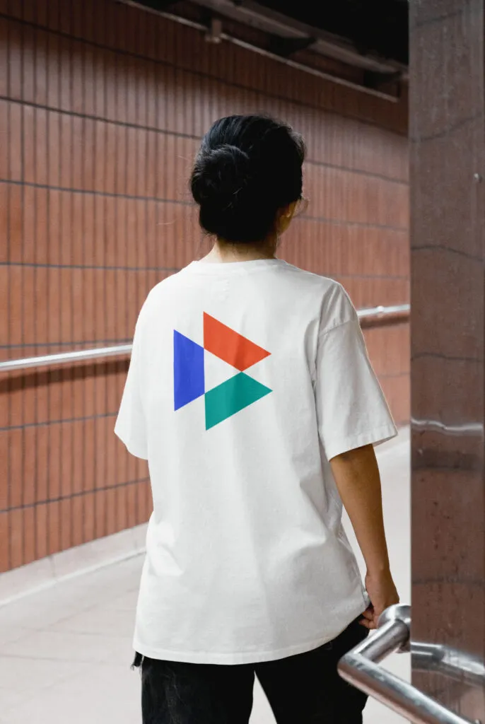 person walking through a brick hallway wearing white t-shirt with a simple 3-color triangular logo on the back