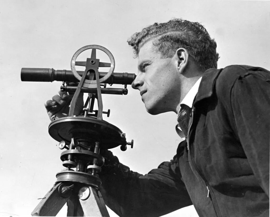 Black and white photo of a man looking through a telescope