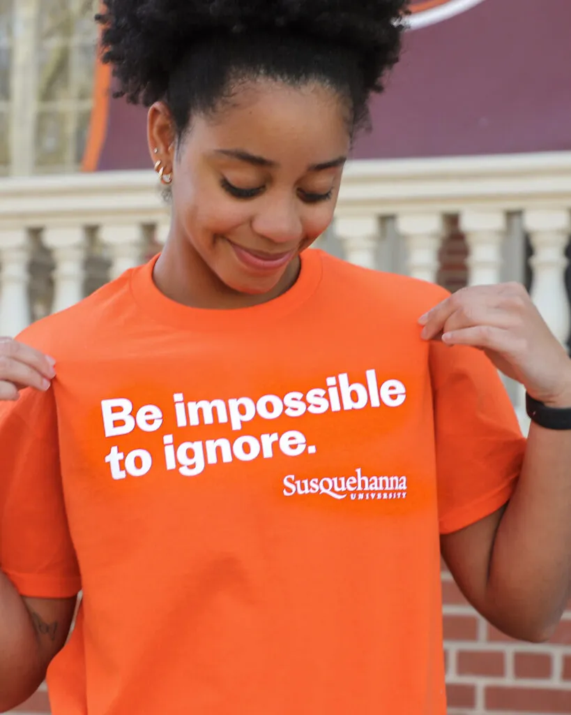 College student smiles at bright orange t-shirt branded for Susquehanna University by J2