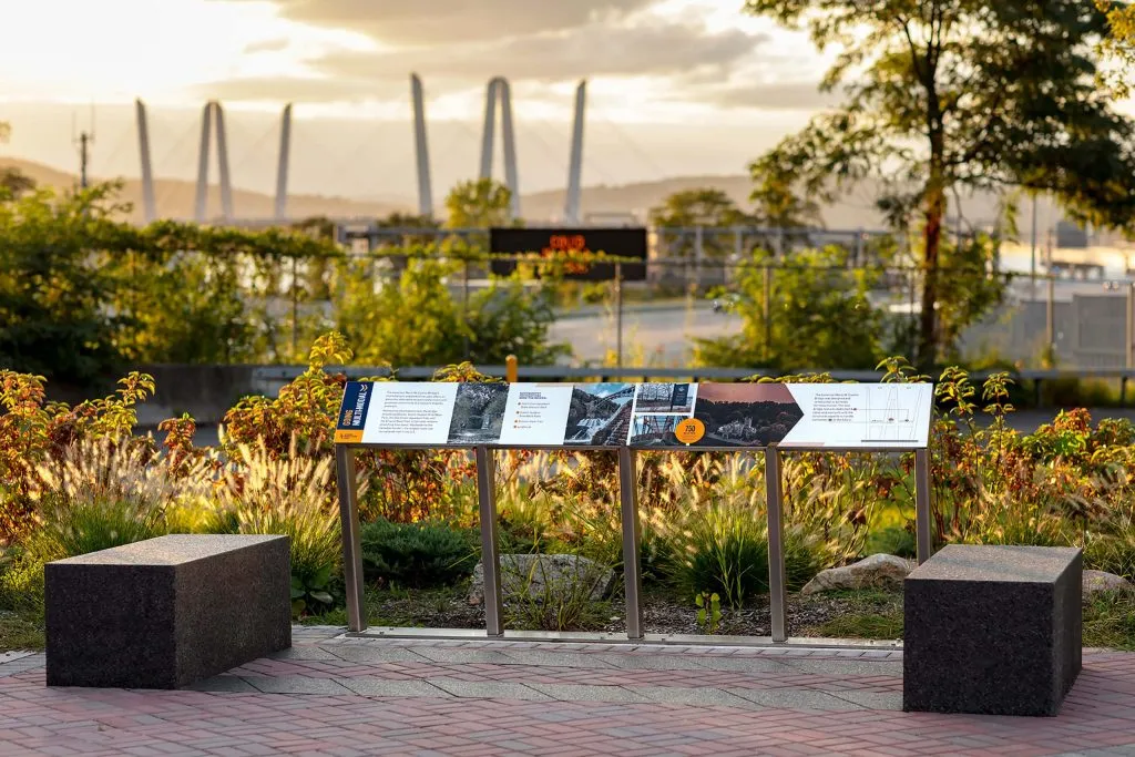 interpretive panel, benches, and landscaping with large suspension bridge in background