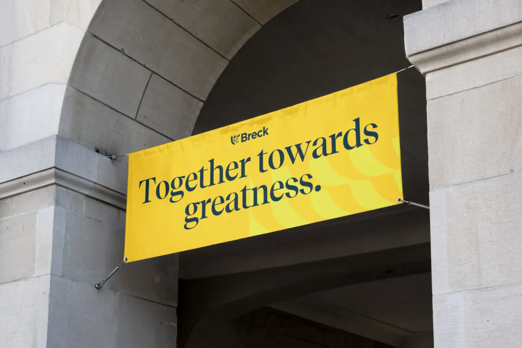 Private school inspirational banner using modern serif font on bright background. The banner is hung from a historic stone building as part of Breck School branding by J2.