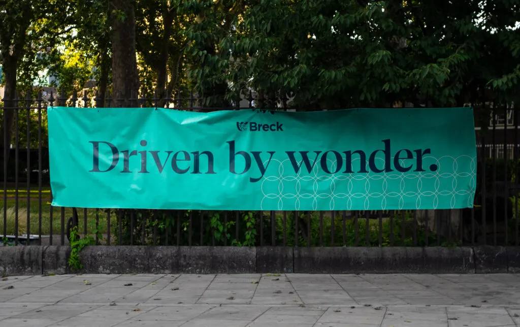 Banner featuring modern serif font on teal background and brand TOV hangs on a garden fence. Branding project for Breck School by J2.