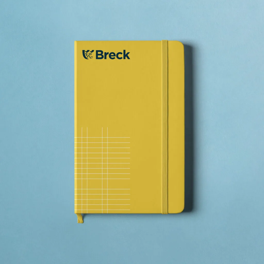 Yellow notebook with private school logo on blue background. Branded swag for Breck School by J2.