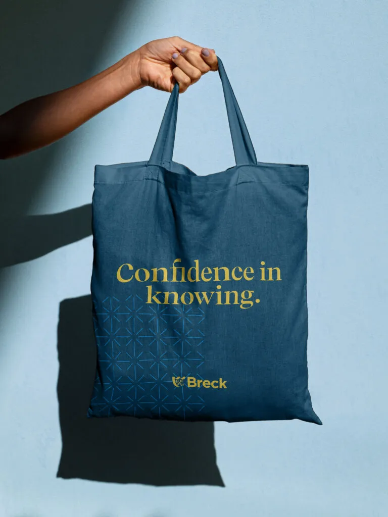 Tote bag with yellow typography on a navy background. Breck School branding by J2.