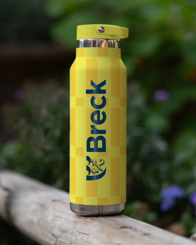 Branded water bottle with school name and logo pictured outside with greenery. Marketing merch design by J2 for Breck School.