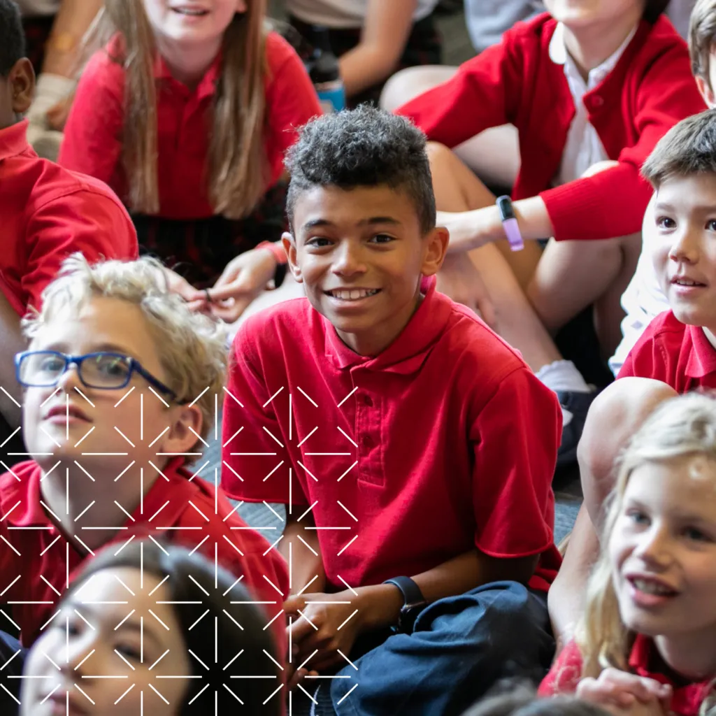 Smiling student in red school uniform sitting at an assembly.