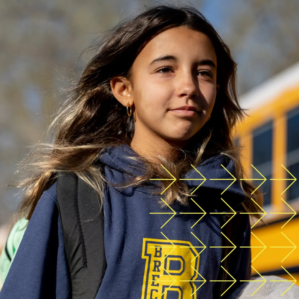 Determined student wearing backpack and branded prep school hoodie walks near school buses.