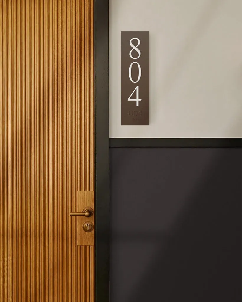 Apartment number sign next to midcentury modern wood door, wayfinding strategy by J2 for The Muse