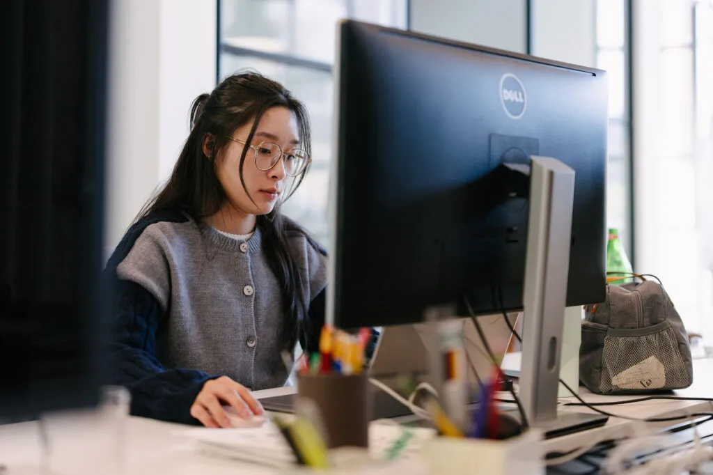 Asian American woman designer working at desk in front of large monitor