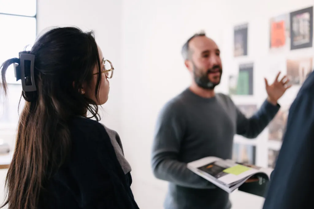 An over-the-shoulder photo of a young designer listening in on a critique being held in a brightly lit design studio