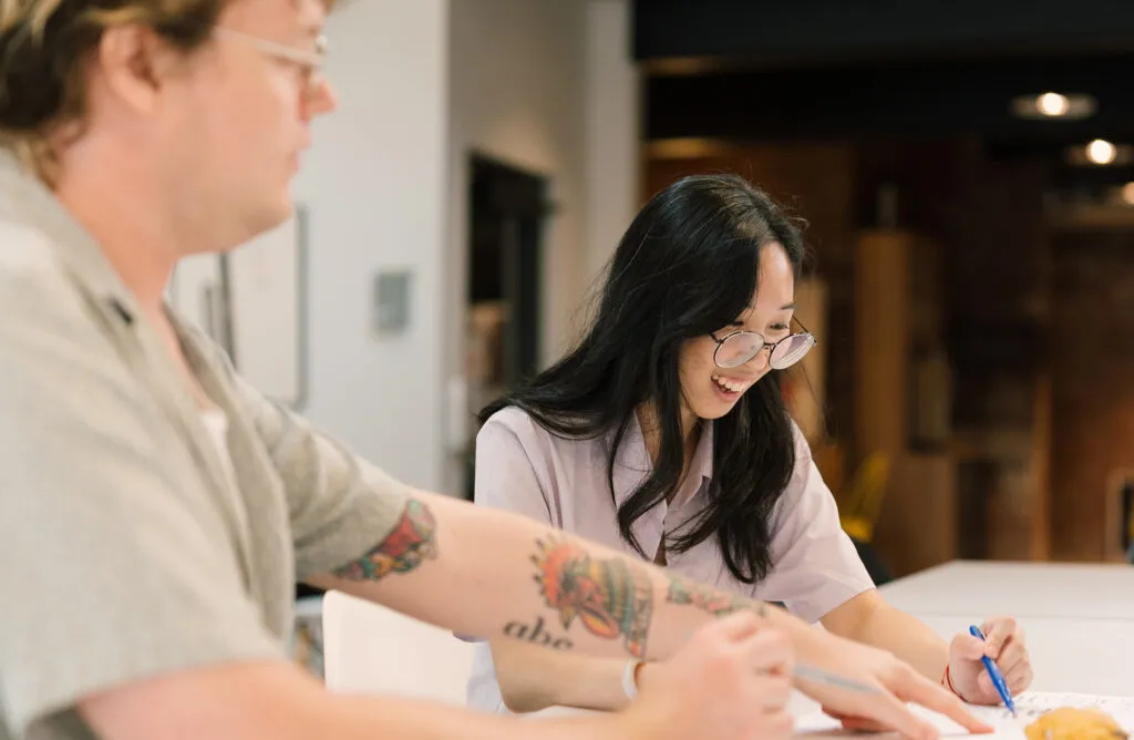 Image of a graphic designer and a design apprentice working together to solve a problem in a well lit office environment